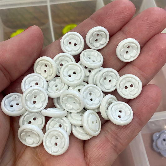 Hand holding white buttons with a container of buttons in the background