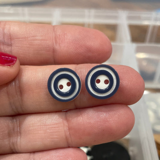 Small round buttons held between fingers with a container of buttons in the background