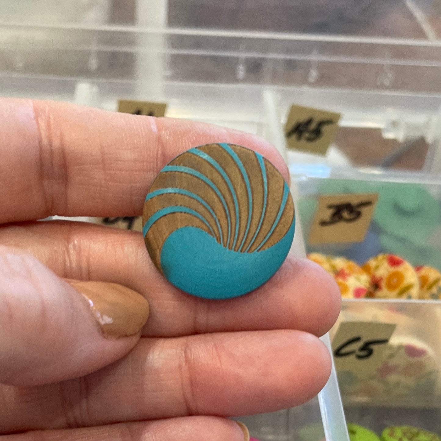 Hand holding a blue and gold decorative item with a display of similar items in the background.