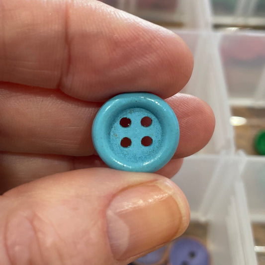 Hand holding a blue button with a container of buttons in the background