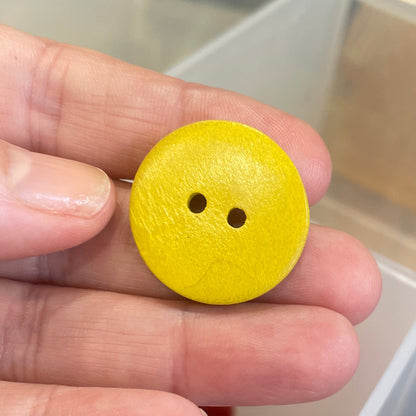 Yellow button held by a hand with a container of buttons in the background