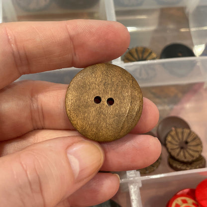Hand holding a gold button with a clear container of assorted buttons in the background