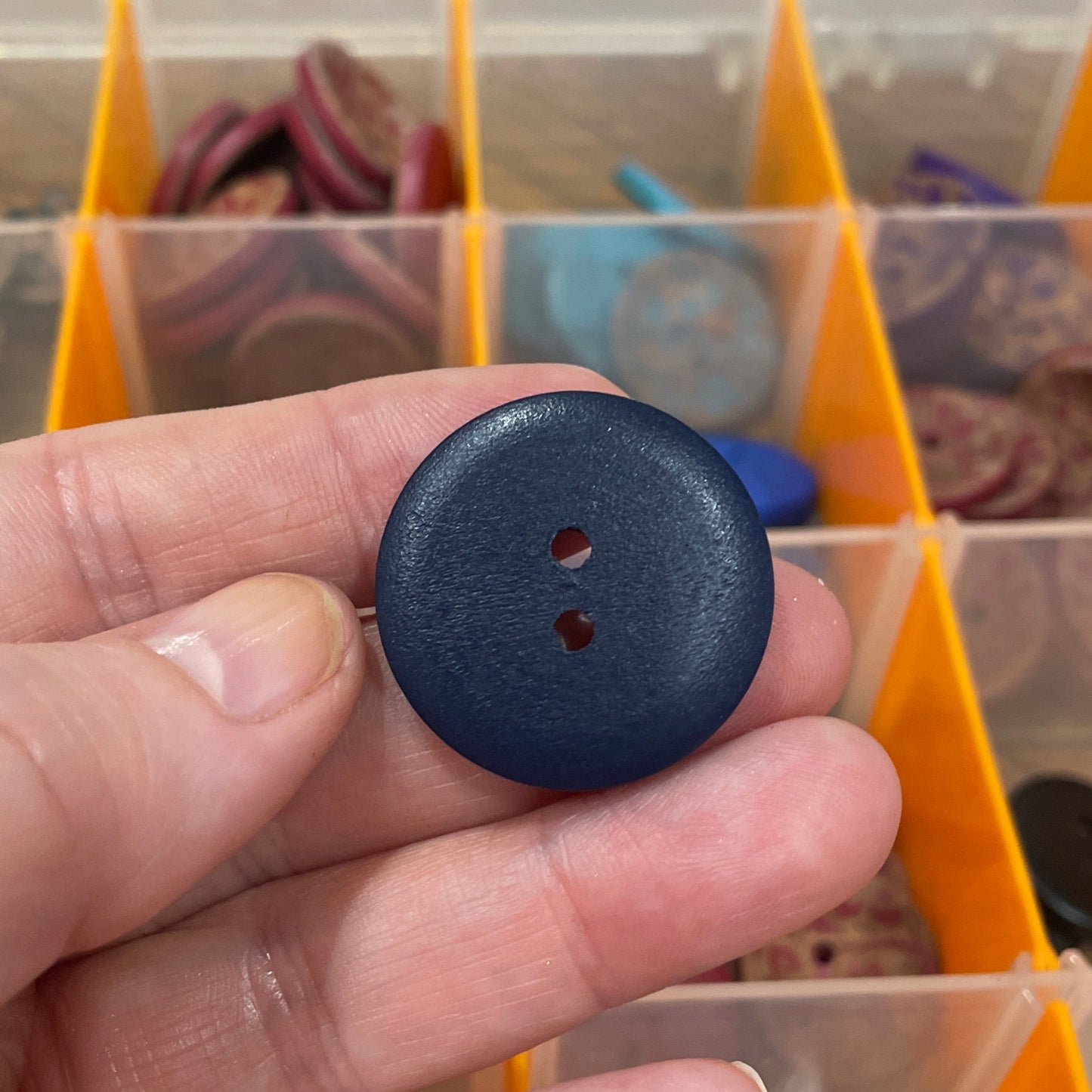 Hand holding a blue button with a background of a button organizer.