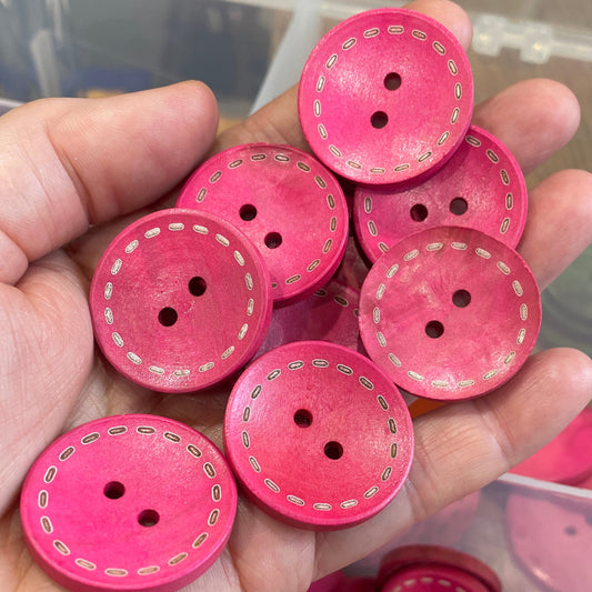 Hand holding pink buttons with a clear container of more buttons in the background