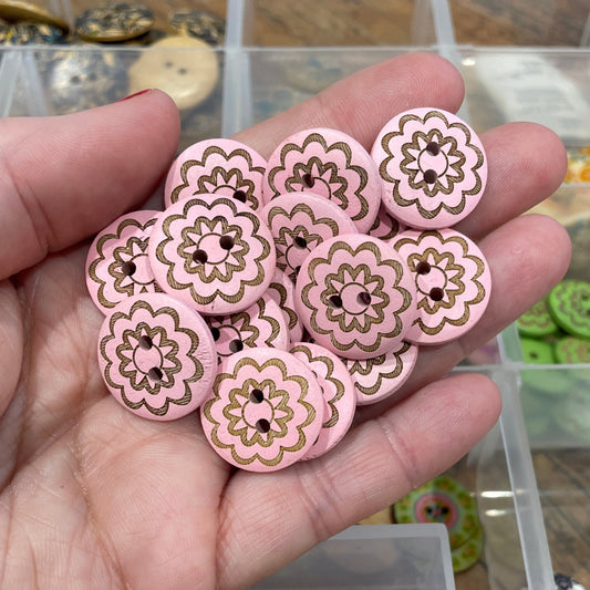 Hand holding pink floral buttons with a container of assorted buttons in the background.