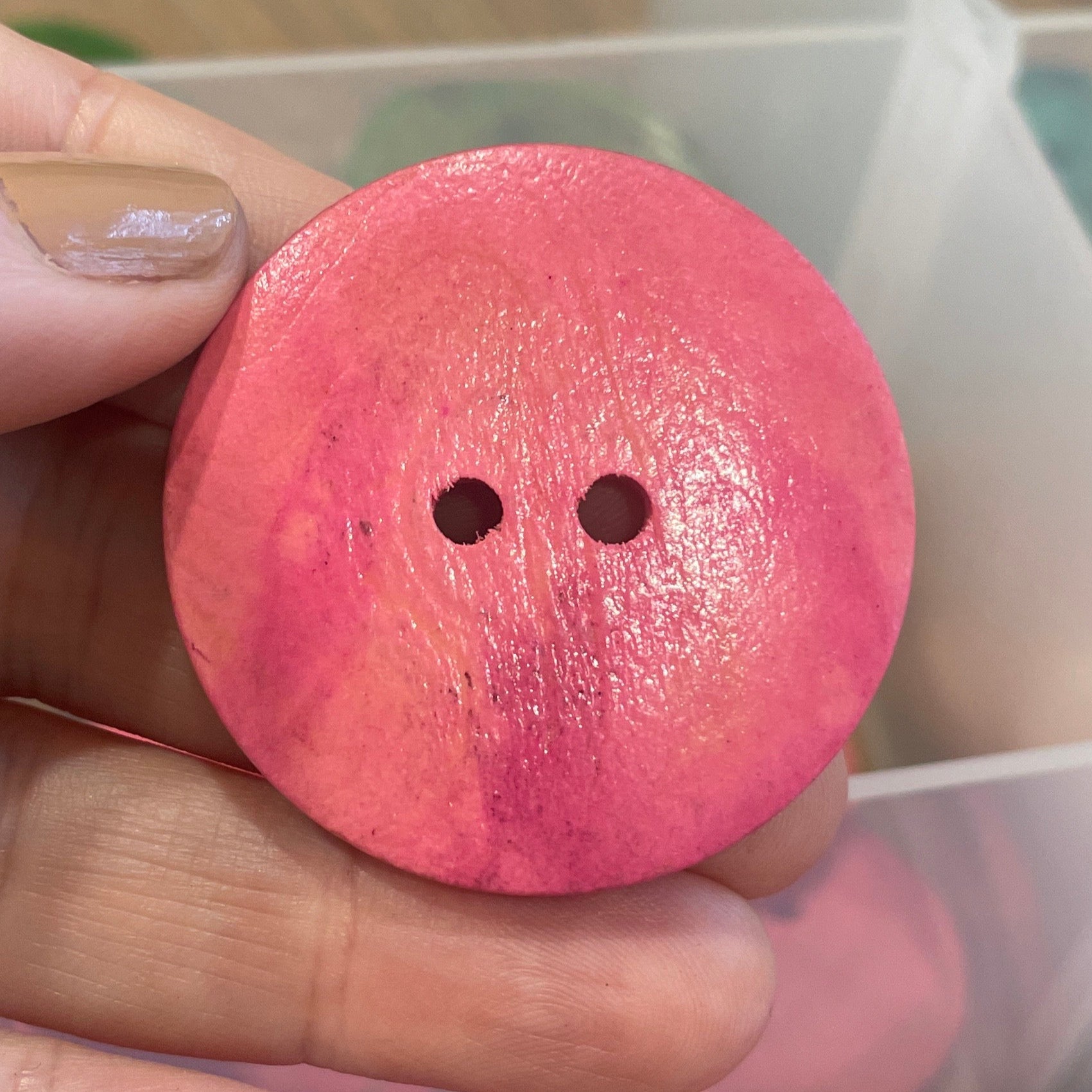 Hand holding a pink button with a container of pink buttons in the background