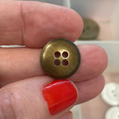 Hand holding a gold button with a blurred background of button collection