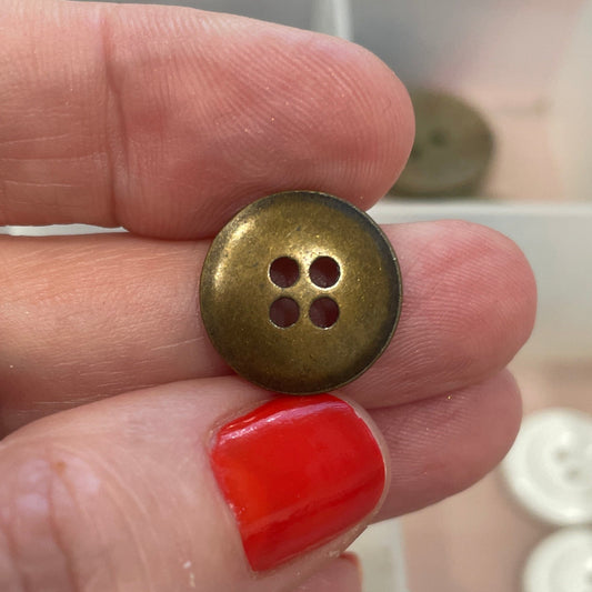 Hand holding a gold button with a blurred background of button collection
