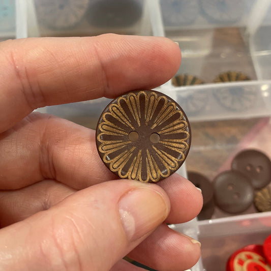 Hand holding a decorative button with a clear container of buttons in the background