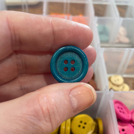 Hand holding a blue button with a container of colorful buttons in the background
