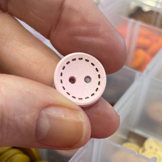Pink button held by a hand with a container of buttons in the background