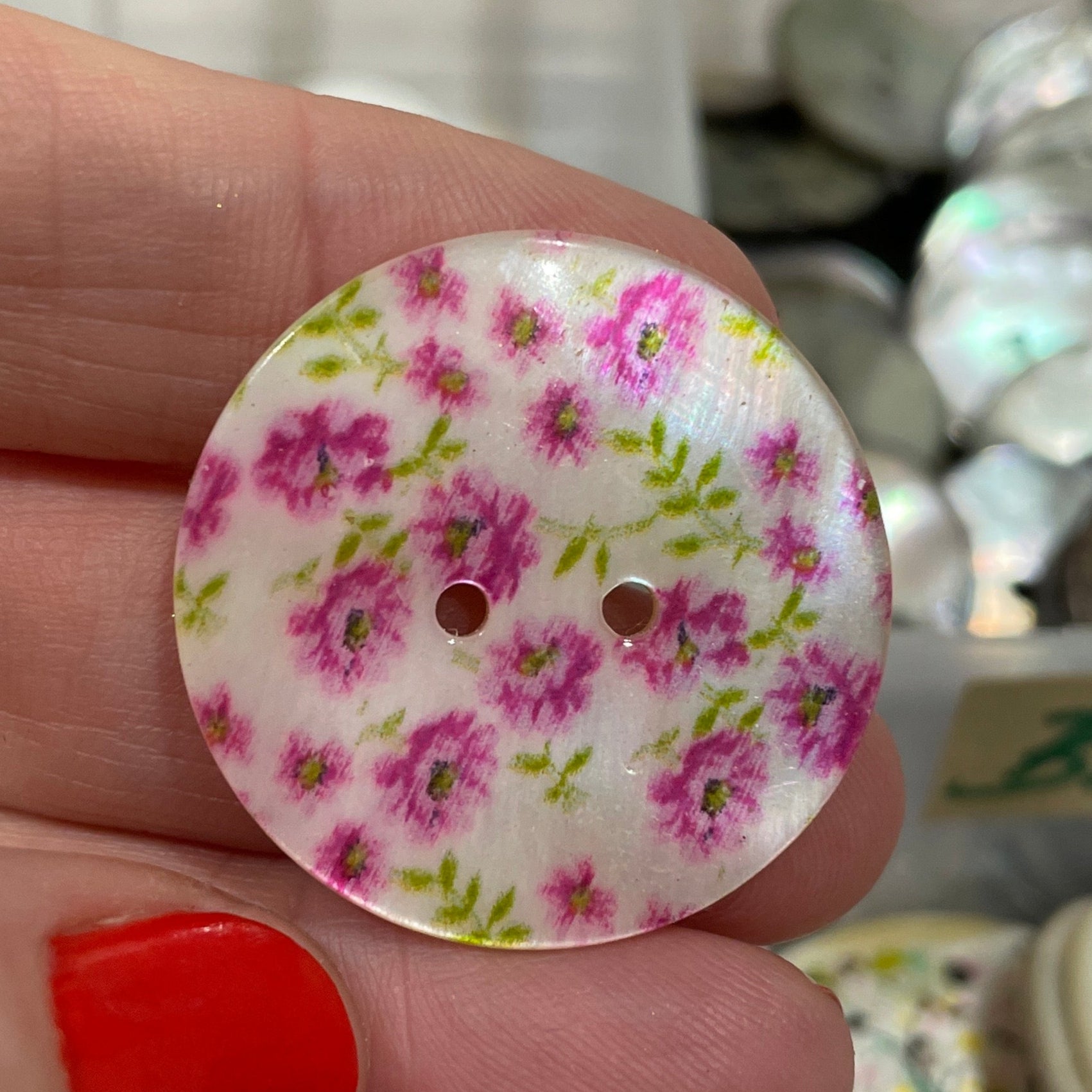 Hand holding a floral button with a blurred background of more buttons.