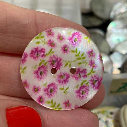 Hand holding a floral button with a blurred background of more buttons.
