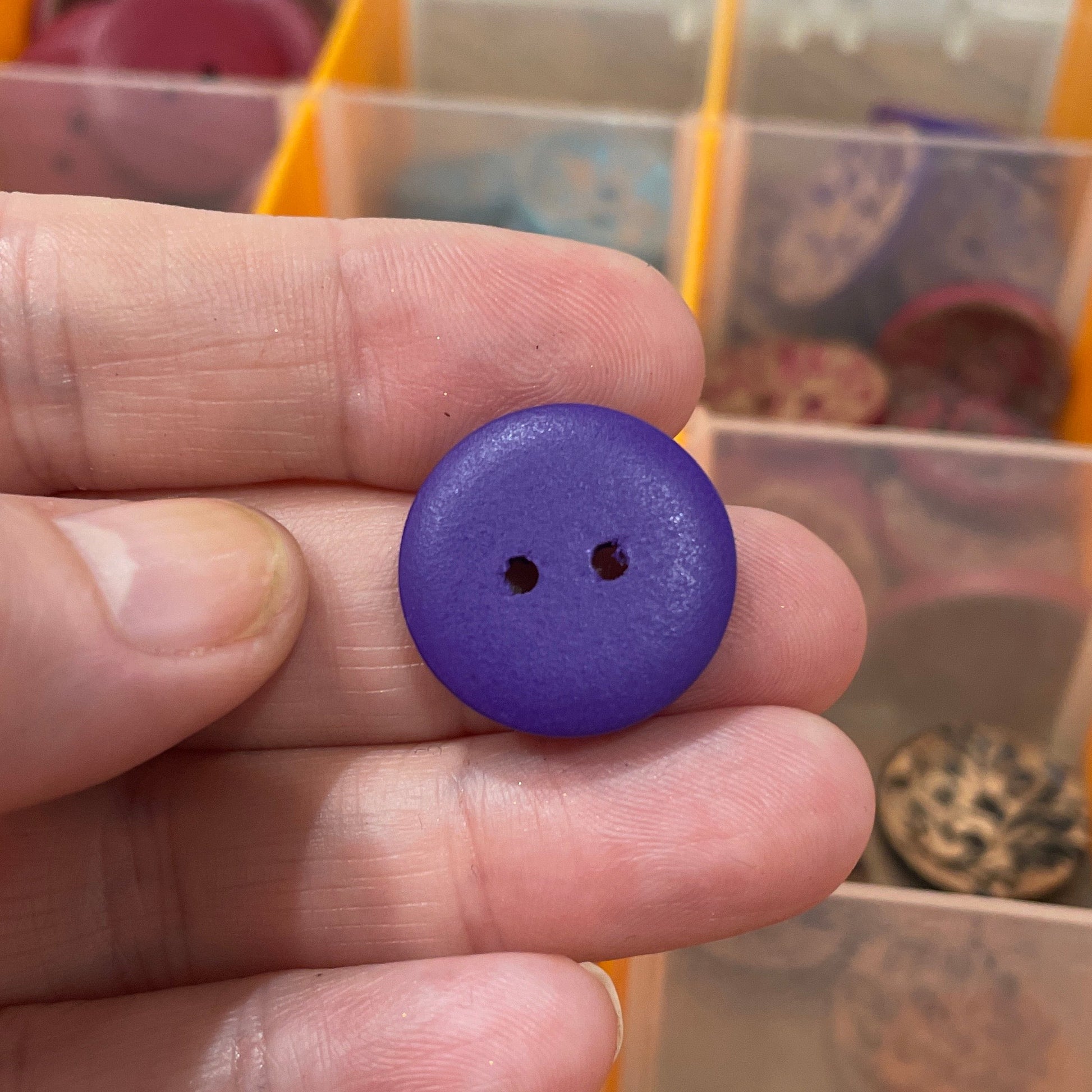 Hand holding a purple button with a background of a button organizer.