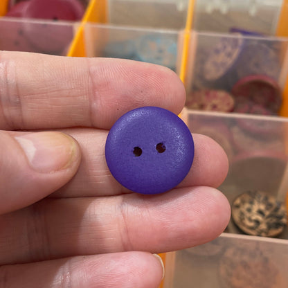 Hand holding a purple button with a background of a button organizer.