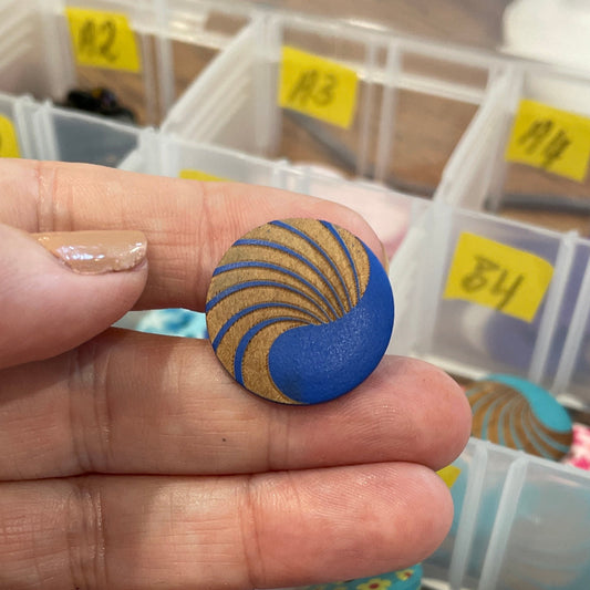 Hand holding a blue button with a yellow pattern against a background of colorful buttons in a container.