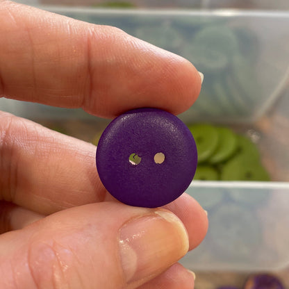Hand holding a purple button with a clear container of buttons in the background