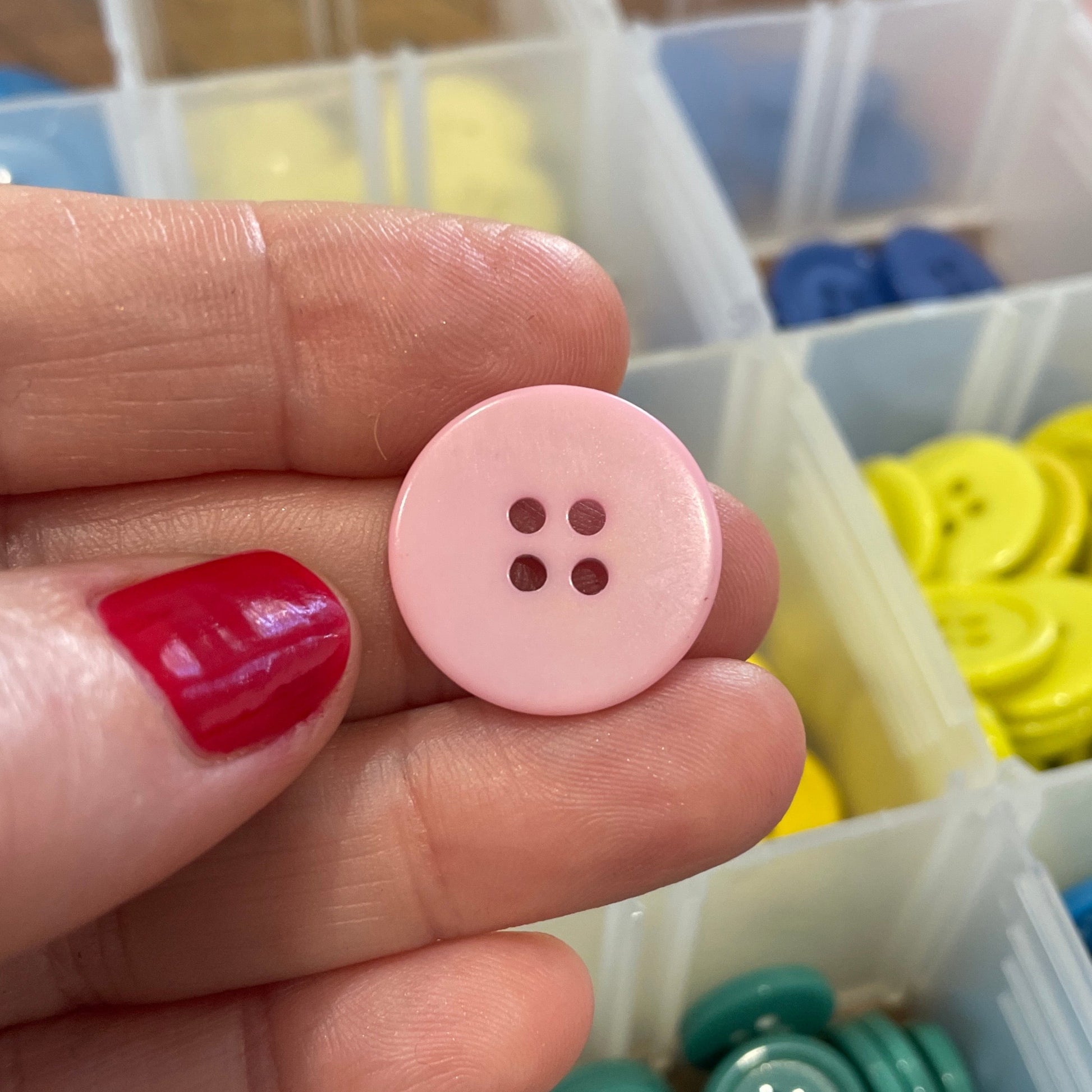 Pink button held between fingers with colorful buttons in a container in the background
