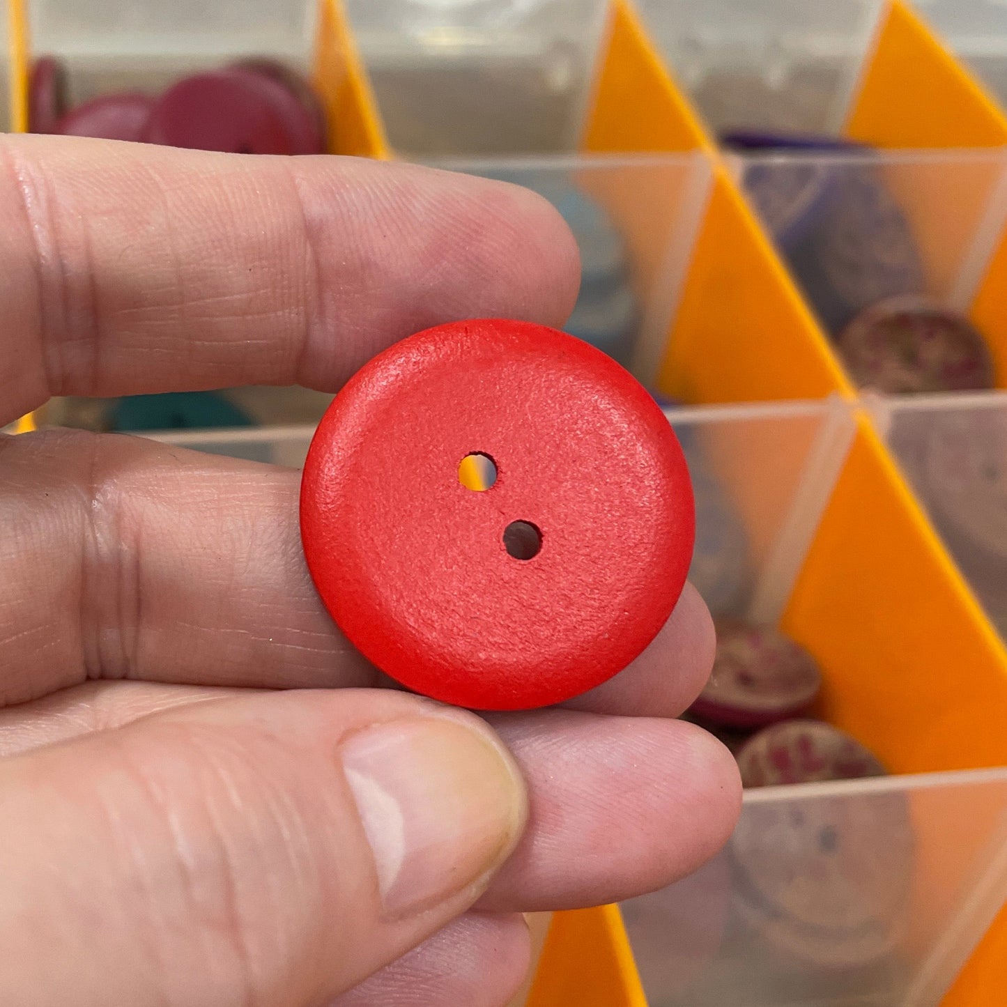 Red button held by a hand with a background of various buttons in an organizer.