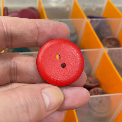 Red button held by a hand with a background of various buttons in an organizer.