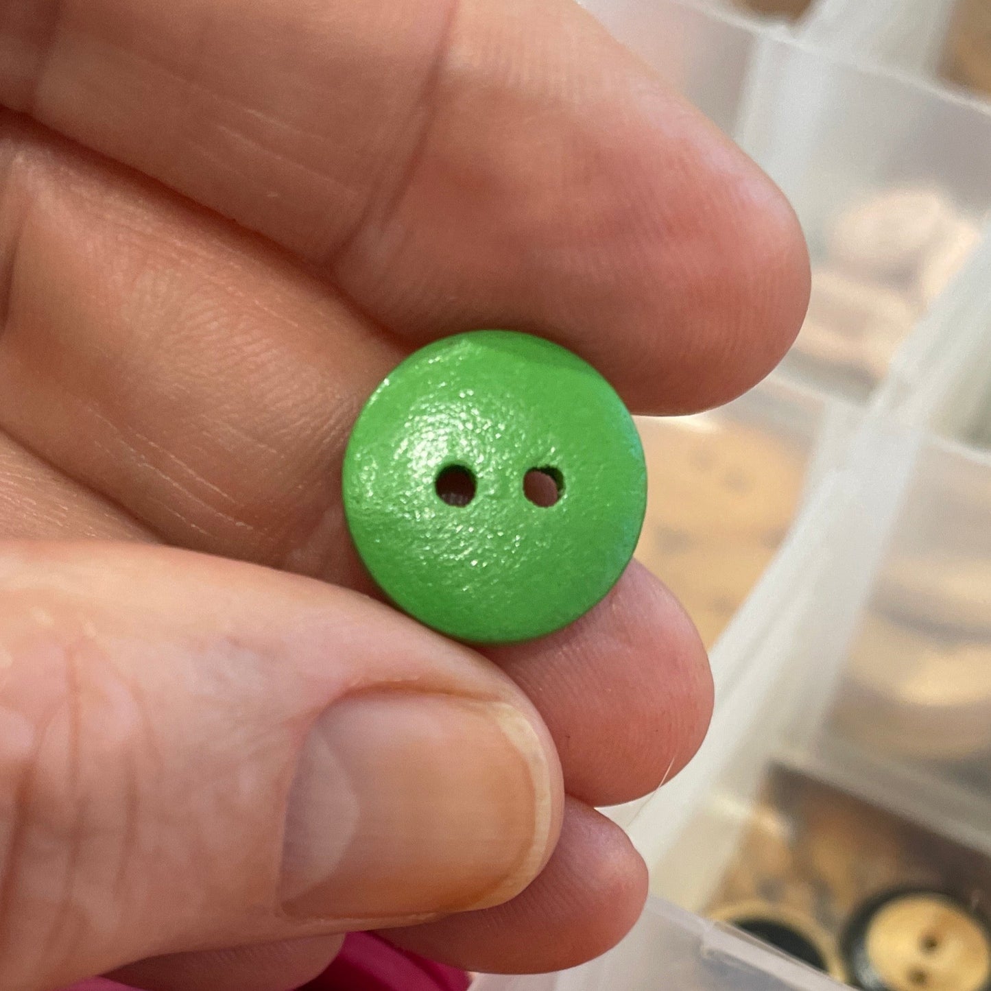 Hand holding a green button with a container of colorful buttons in the background