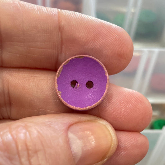 Hand holding a purple button with a container of buttons in the background