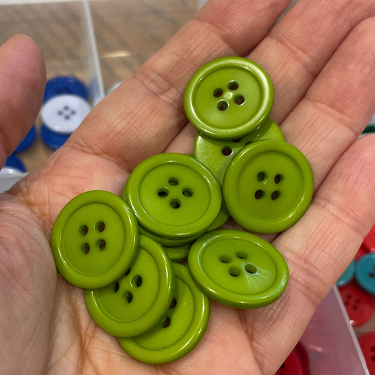 Hand holding green buttons with a container of buttons in the background