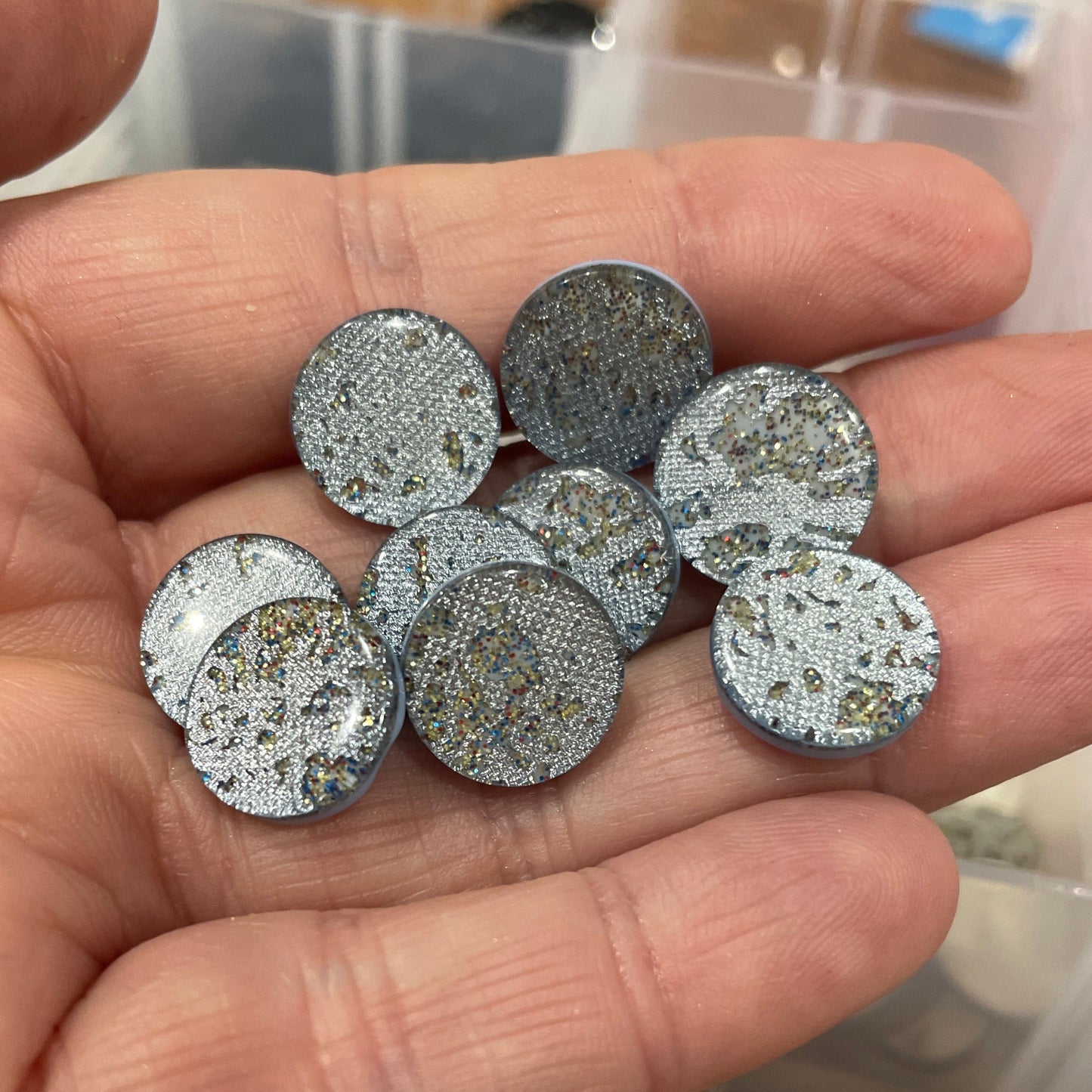 Hand holding silver glittery round objects with a container of similar objects in the background.