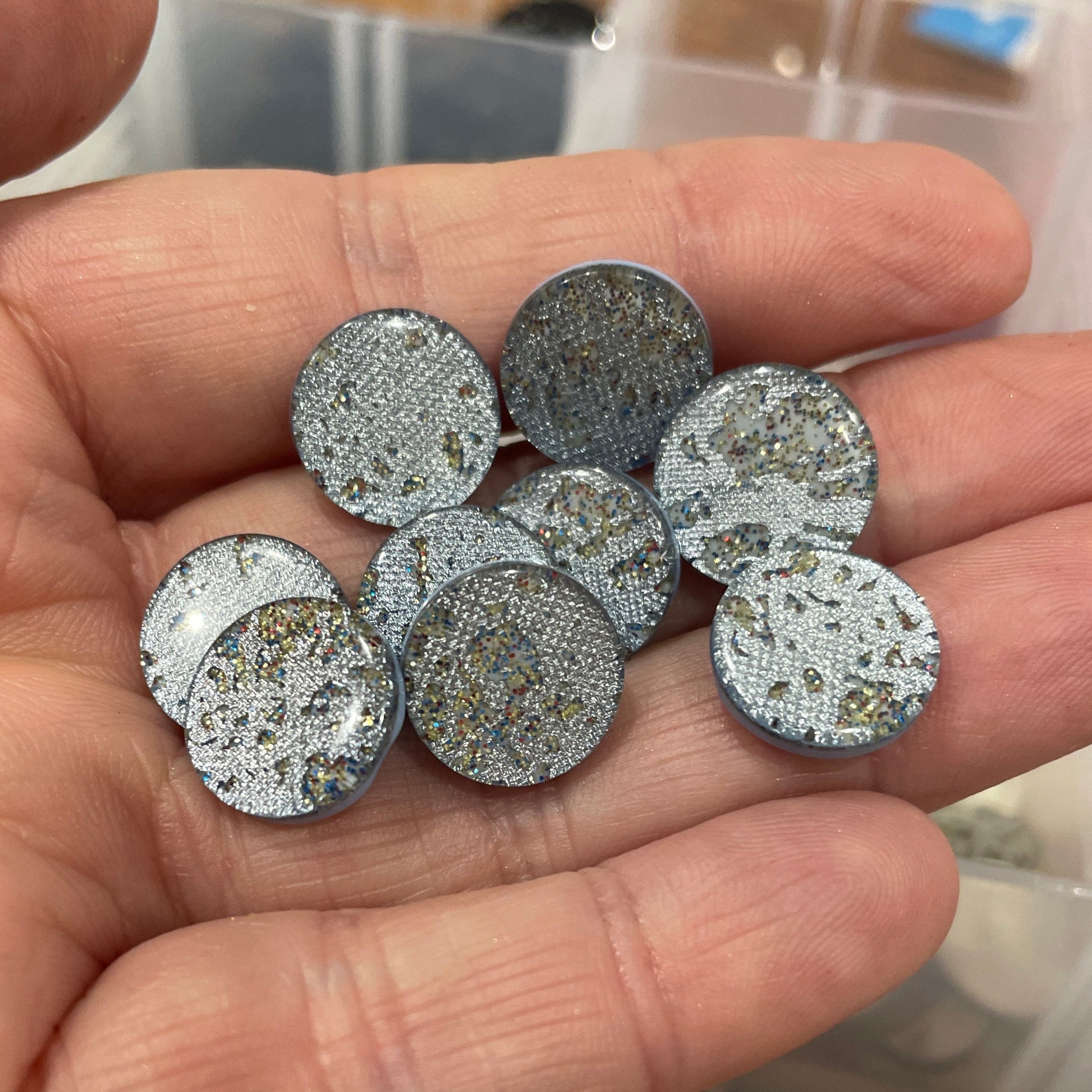 Hand holding silver glittery round objects with a container of similar objects in the background.