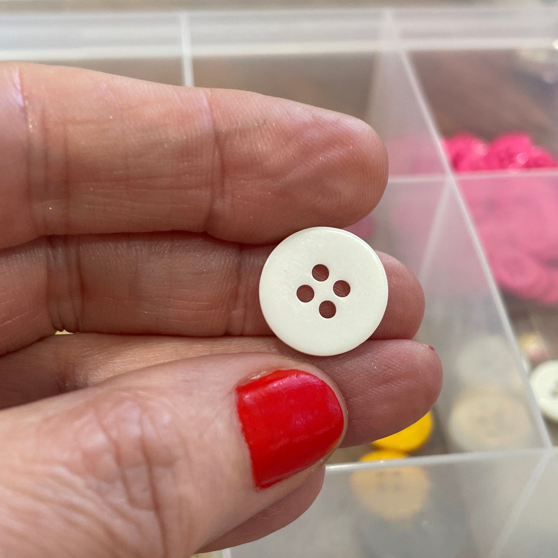 White button held between fingers with a container of colorful buttons in the background