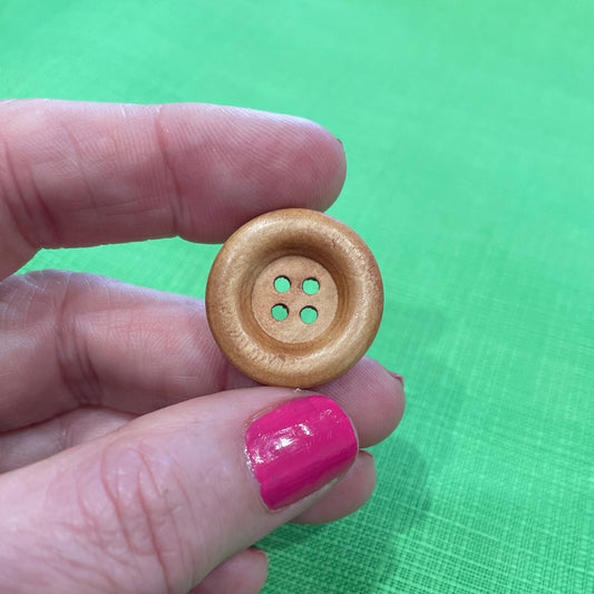 Hand holding a wooden button against a green background