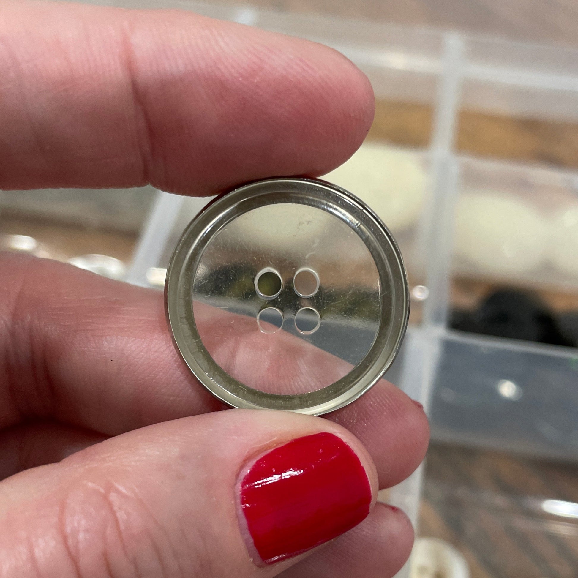 Hand holding a button with a clear container of buttons in the background