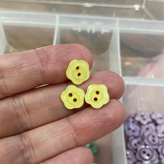 Hand holding small yellow buttons with a container of assorted buttons in the background