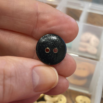 Black button held between fingers with colorful buttons in a container in the background