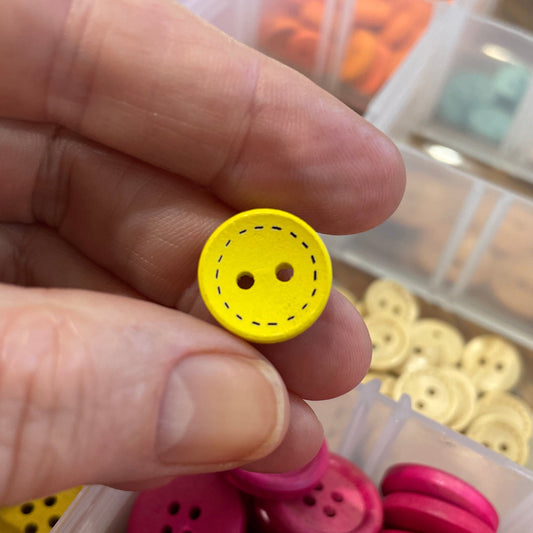 Yellow button held by a hand with a container of pink buttons in the background