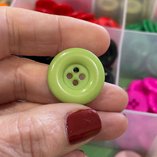 Hand holding a green button with a colorful button collection in the background