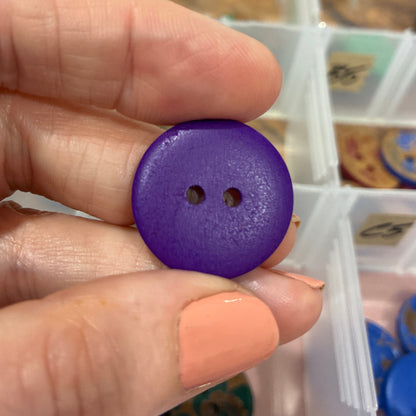 Hand holding a purple button with a container of buttons in the background