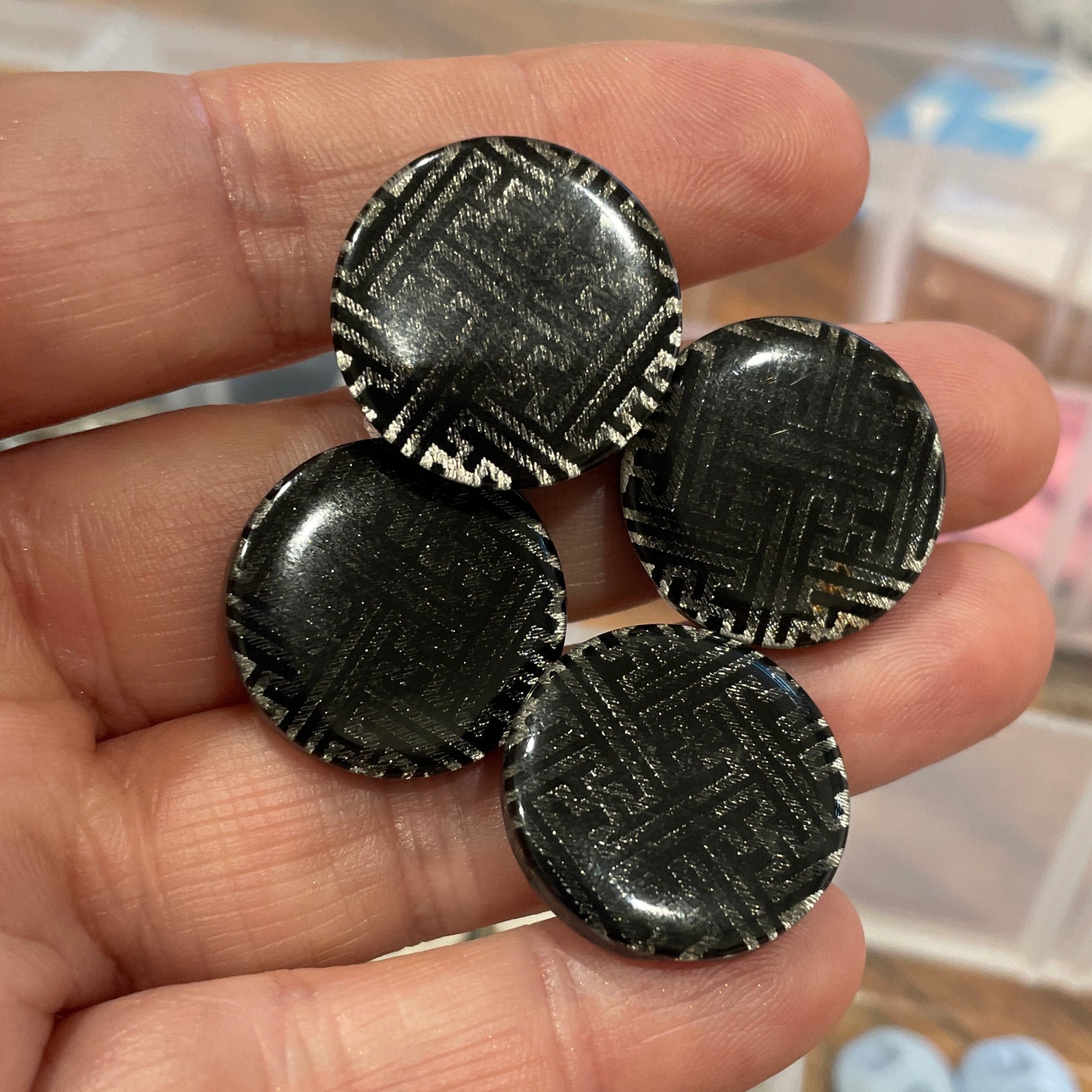 Black buttons held in a hand with a blurred background of containers with various items.