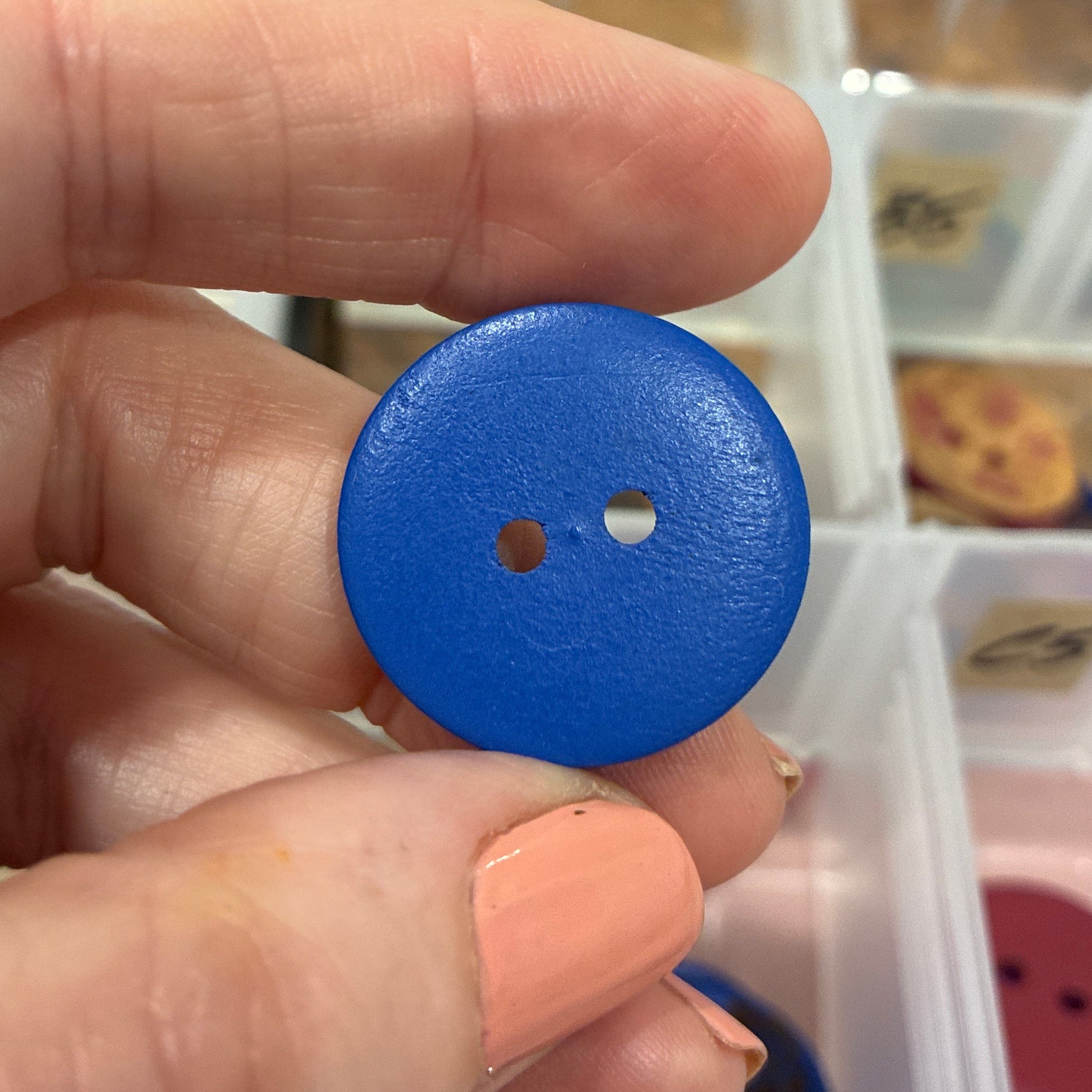 Hand holding a blue button with a blurred background of a button organizer.