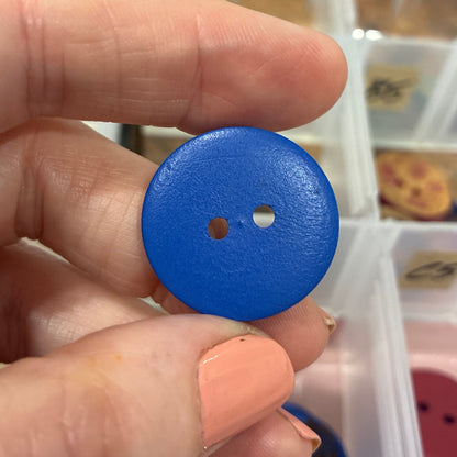 Hand holding a blue button with a blurred background of a button organizer.