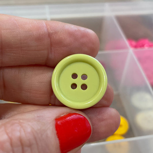 Hand holding a yellow button with a clear container of buttons in the background