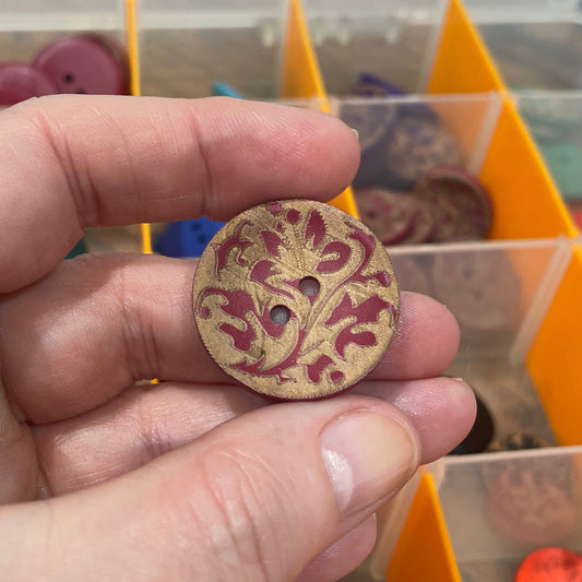 Hand holding a decorative button in front of a container with various buttons.