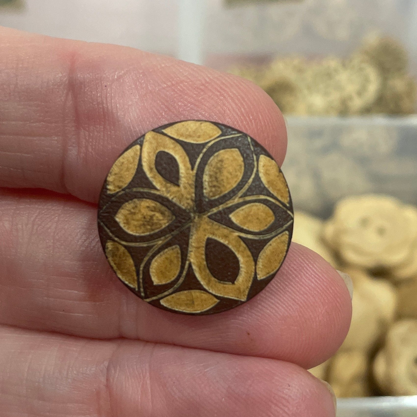 Hand holding a decorative button with a blurred background of button collection
