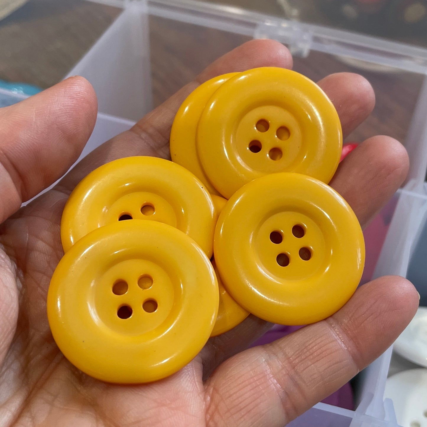 Hand holding four yellow buttons with a container of buttons in the background