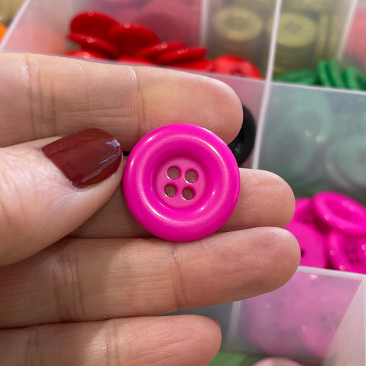 Hand holding a pink button with a container of colorful buttons in the background