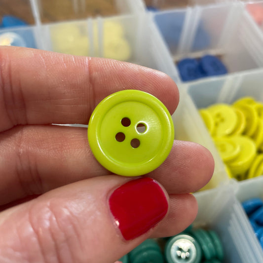 Hand holding a yellow button with a colorful array of buttons in the background