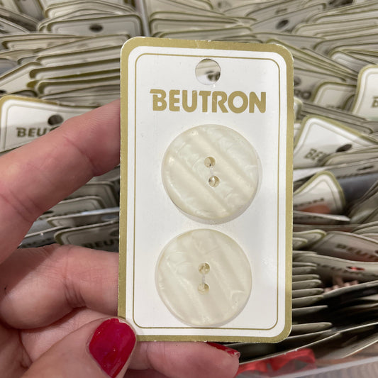 Button card with 'Beutron' branding held by a hand against a background of similar cards.