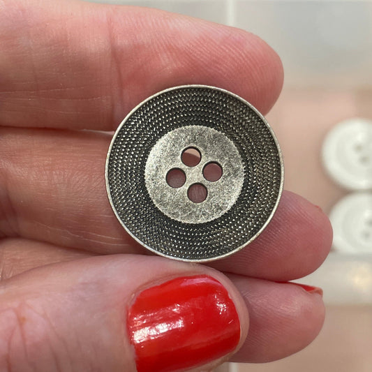 Hand holding a silver button with a blurred background of button collection
