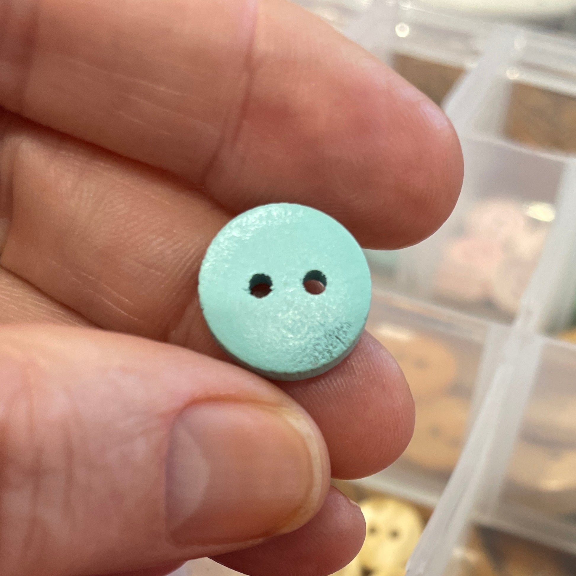 Hand holding a light blue button next to a container of colorful buttons.