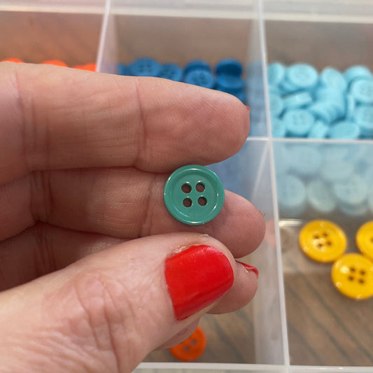Hand holding a green button with a clear container of colorful buttons in the background